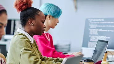 Drei Personen arbeiten an Laptops in einem modernen Büro.